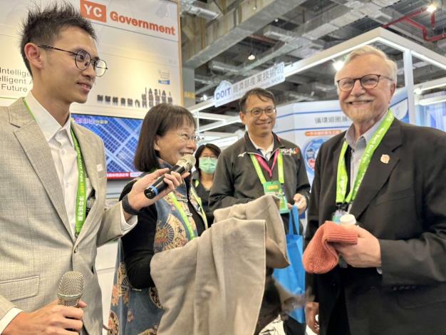 謝副縣長向國際智慧城市組織參訪團展示使用海洋回收環保素材(海毛紗)製成的圍巾